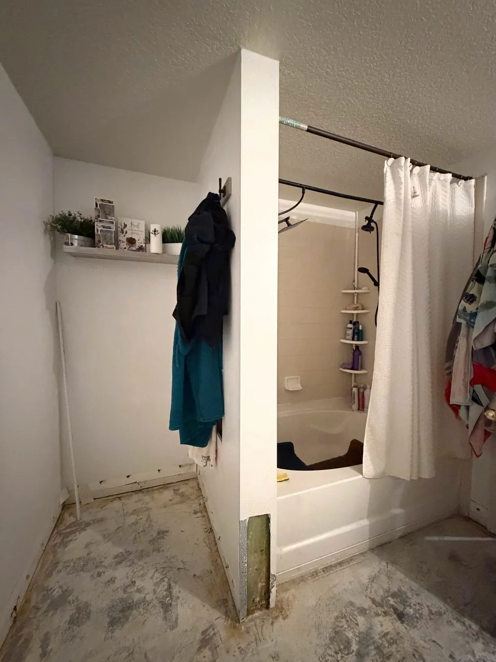 Unused corner beside the original tub and shower, with exposed flooring and a removed section of wall finish.