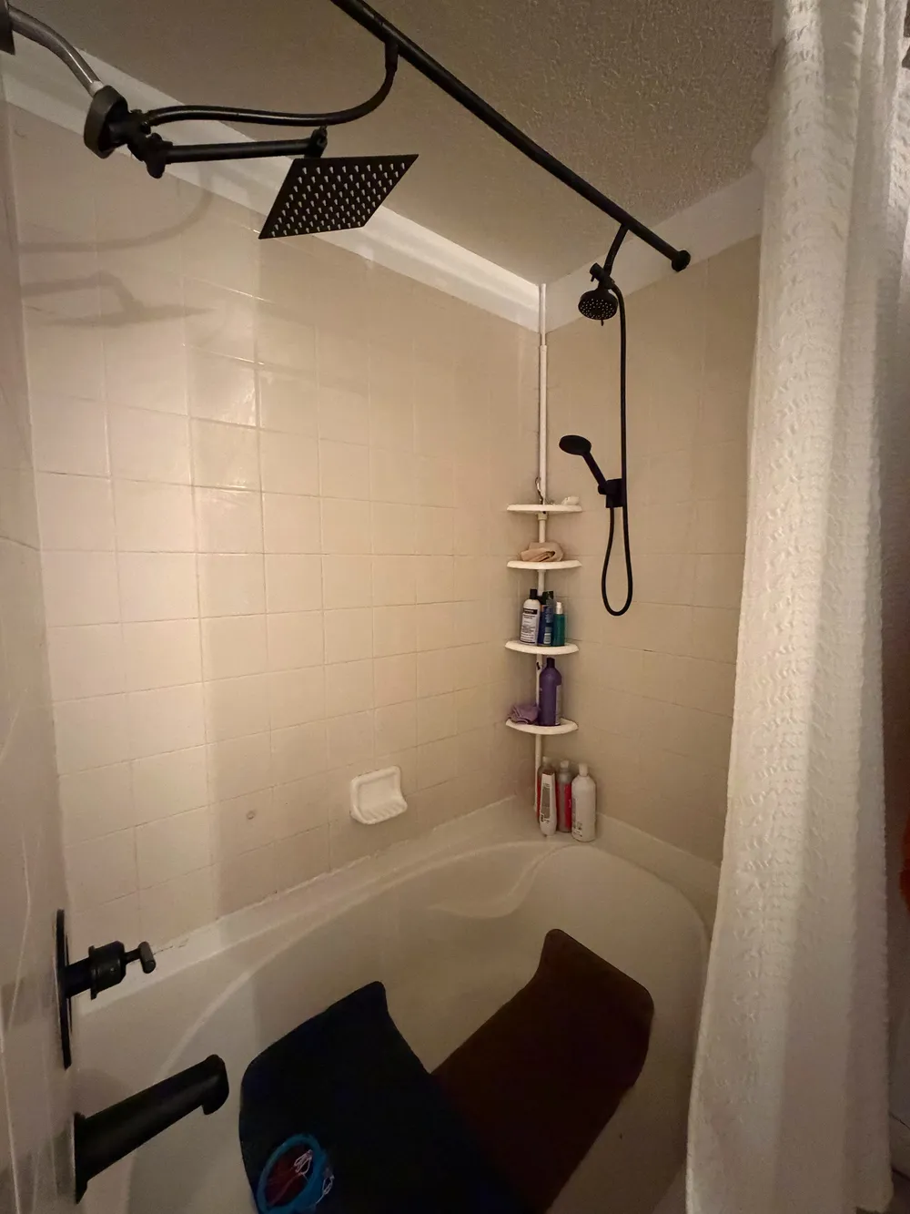 Original compact tub and shower enclosure with white surround, curtain rod, and black fixtures.