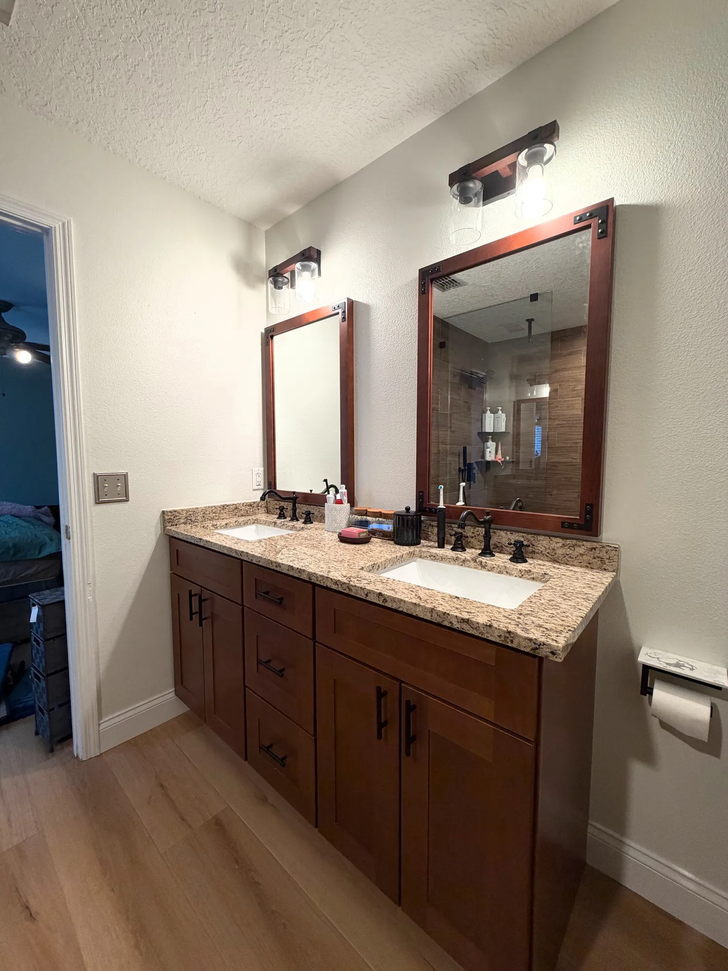 Double vanity with rich wood cabinetry, two undermount sinks, a stone countertop, center drawers, and dark hardware.