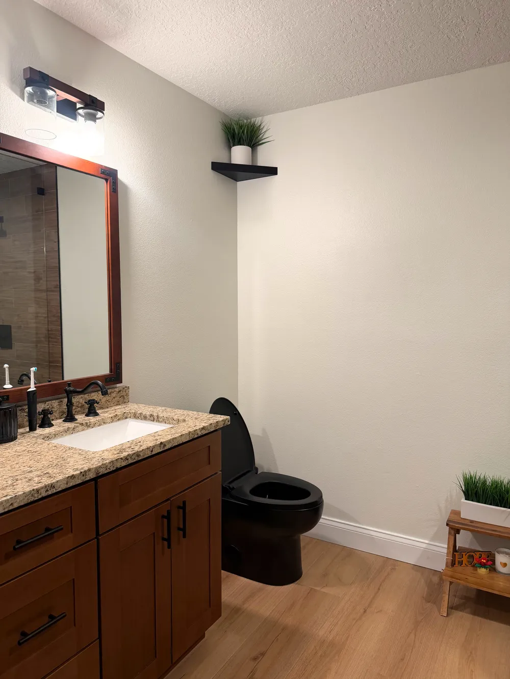 Finished bathroom corner with the wood double vanity, black toilet, light flooring, and wall shelving.