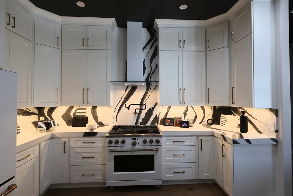 Blackwater range beneath a slim hood, surrounded by white cabinetry and a full-height veined quartz backsplash.