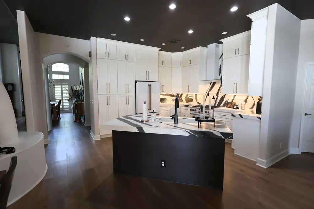 Blackwater kitchen with a dark island, ceiling-height white cabinets and bold veined quartz surfaces.