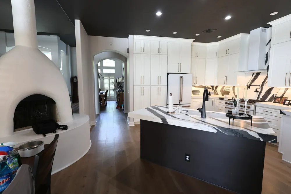 Blackwater kitchen island and white cabinetry beside the fireplace and wide-plank flooring.
