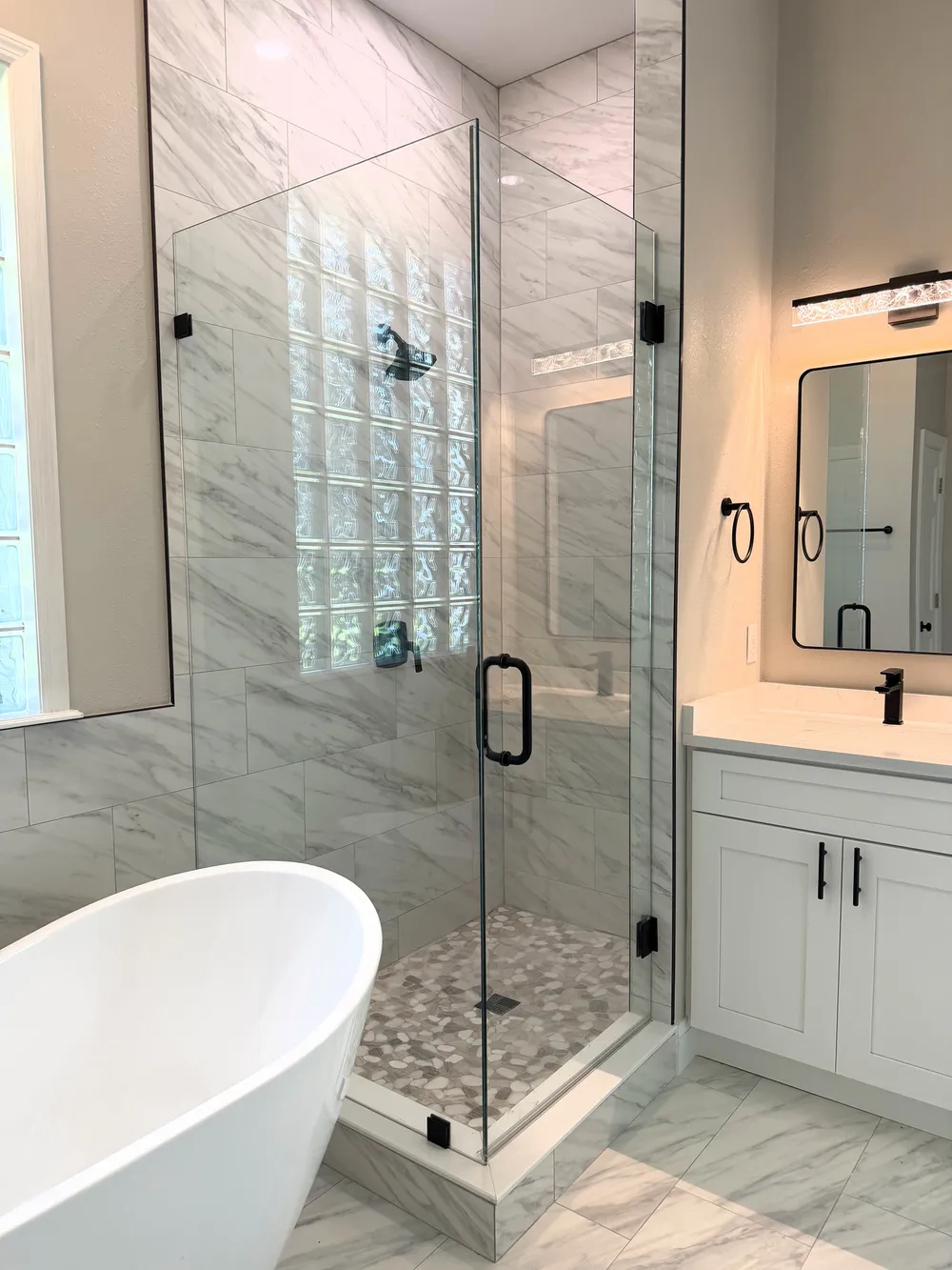 Freestanding tub beside a tiled shower with frameless glass and black fixtures.