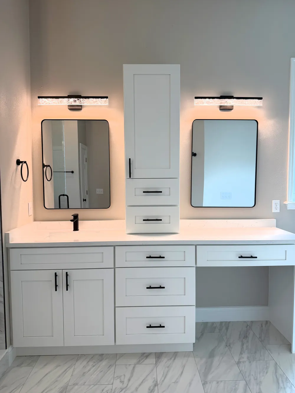 White Estancia vanity with a central storage tower, black-framed mirrors and a dedicated makeup area.