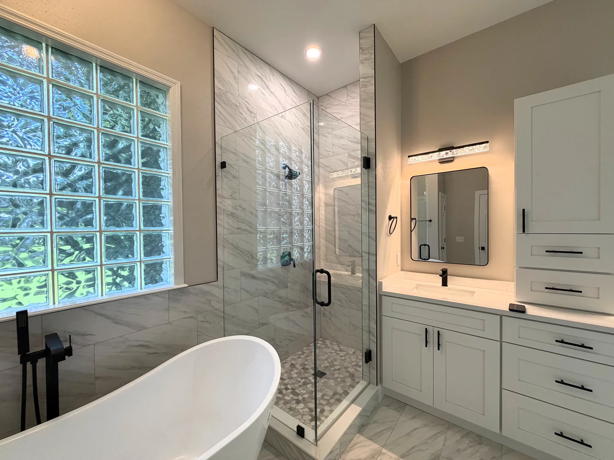 Freestanding tub, frameless shower and white vanity beside a glass-block window in the Estancia bathroom.
