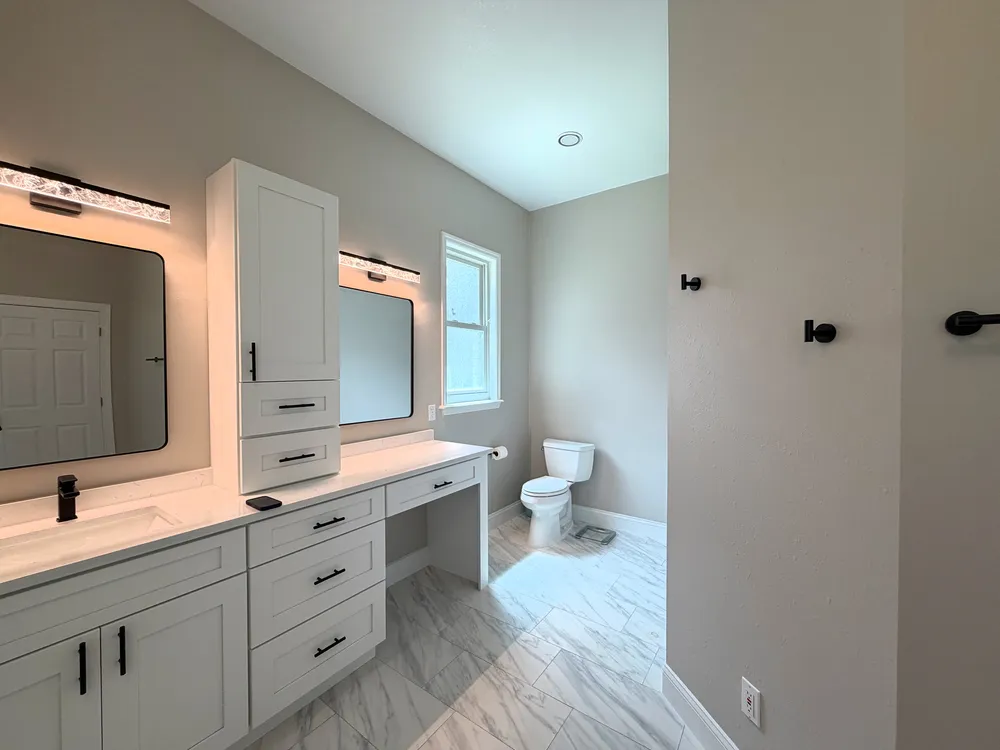 Long white vanity and makeup counter leading toward the Estancia bathroom window and toilet.