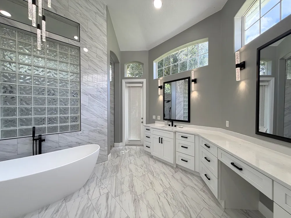 White vanity and makeup counter with black-framed mirrors and wall sconces beside the freestanding tub in The Grand Revival bathroom.
