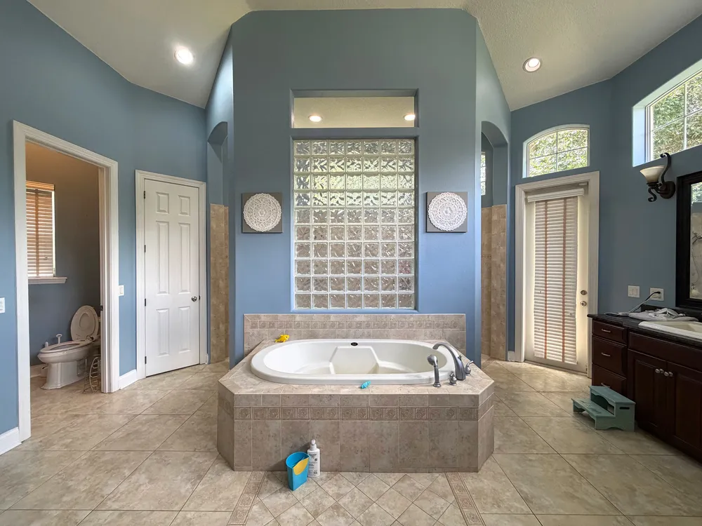 Original built-in jetted bathtub and tiled deck beneath the glass-block wall in The Grand Revival bathroom.