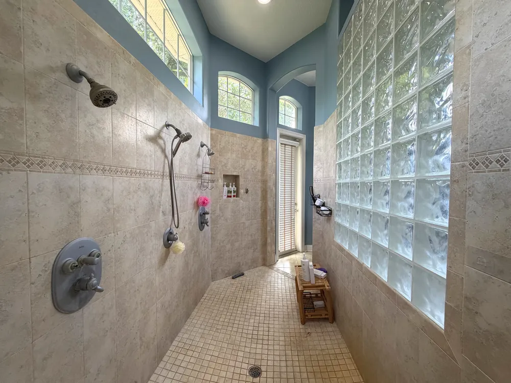 Original walk-in shower with beige wall tile, two shower stations and glass block in The Grand Revival bathroom.