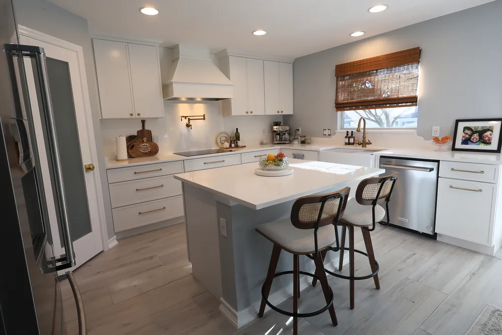 Finished kitchen with white cabinetry, a decorative range hood, quartz surfaces, brass fixtures, and a gray island with two stools.