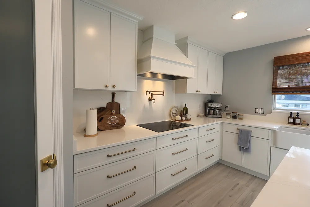 White kitchen cabinetry and brass pulls surrounding a decorative range hood, pot filler, and full-height quartz backsplash.