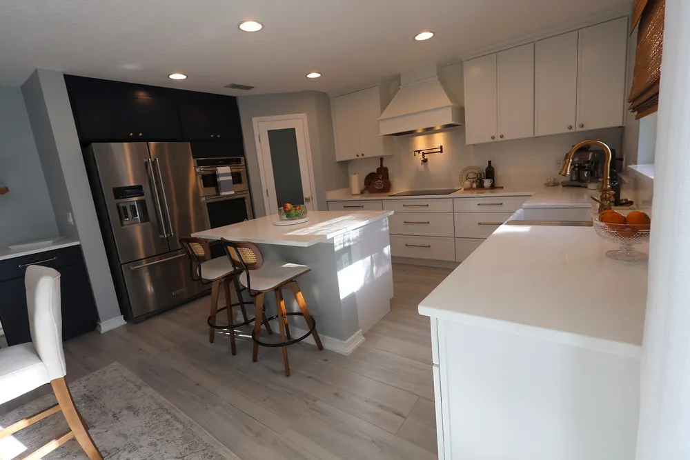 Reverse kitchen view showing the island seating, dark appliance-wall cabinetry, white cooking-wall cabinets, and the adjoining dry bar.