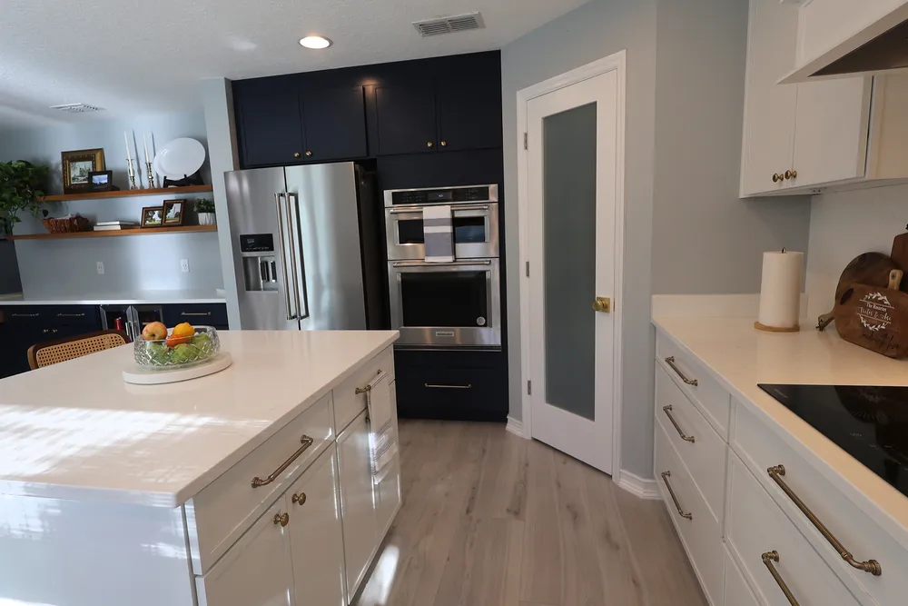 Kitchen aisle between the quartz island with white drawers and the cooking wall, facing dark cabinetry around the refrigerator and wall oven.